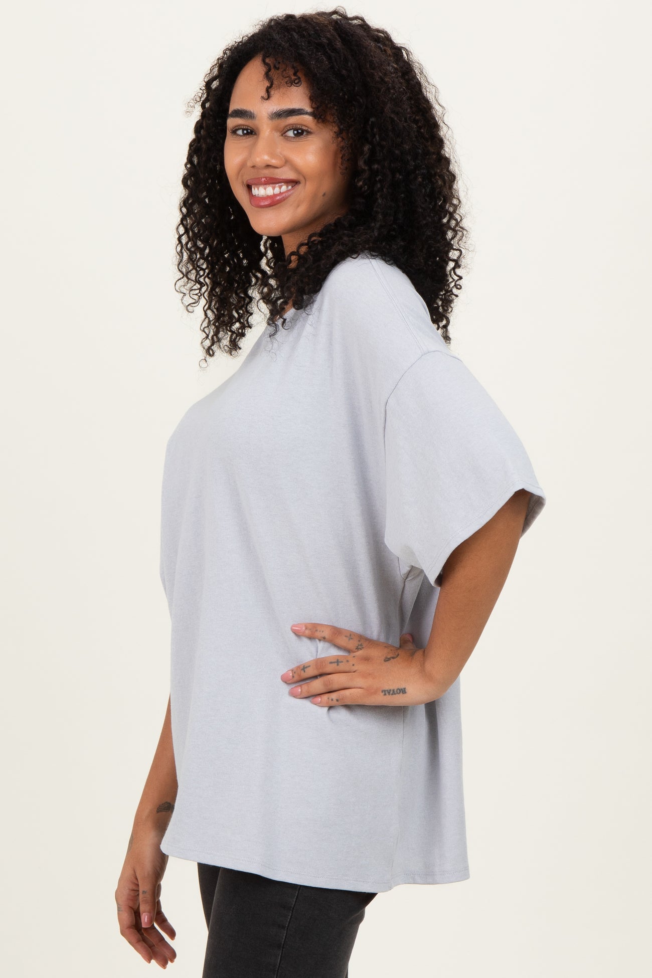 woman wearing a light gray oversized t-shirt and black jeans, smiling with curly hair