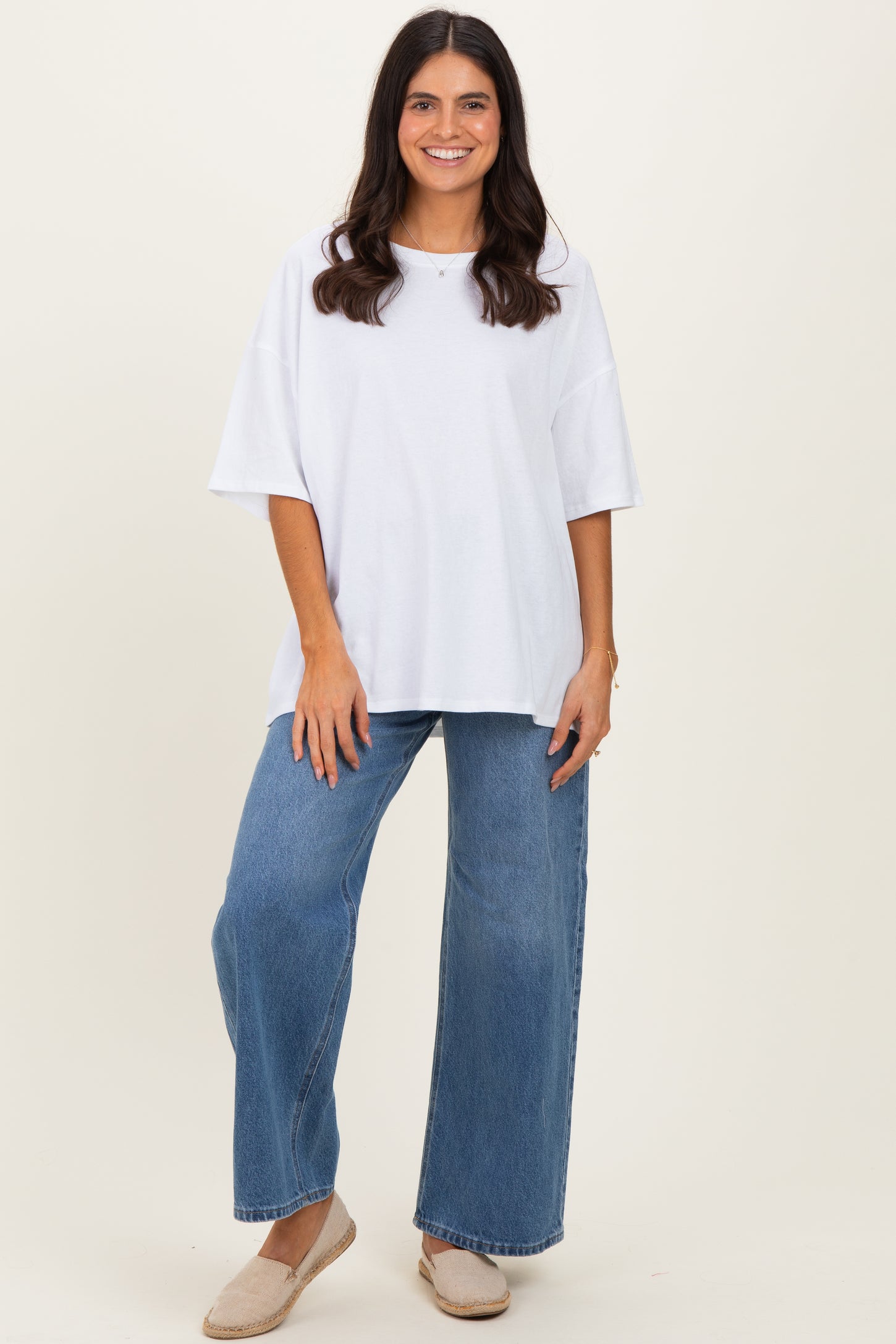 woman wearing a white oversized t-shirt and wide-leg blue jeans, standing and smiling