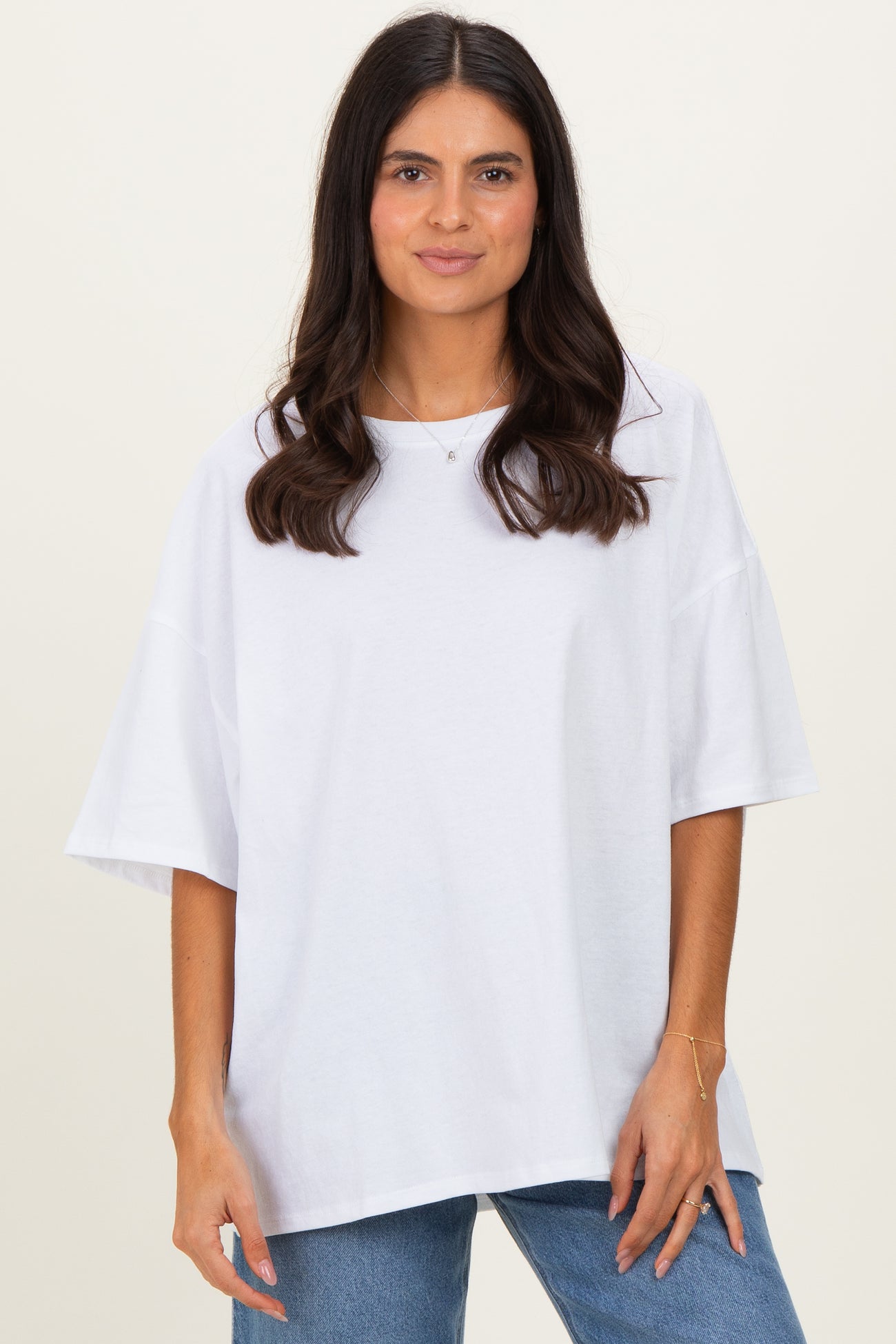 woman wearing a white oversized t-shirt with short sleeves and a relaxed fit, standing against a light background