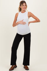 woman wearing a white sleeveless maternity top and black wide-leg pants, smiling and holding her baby bump