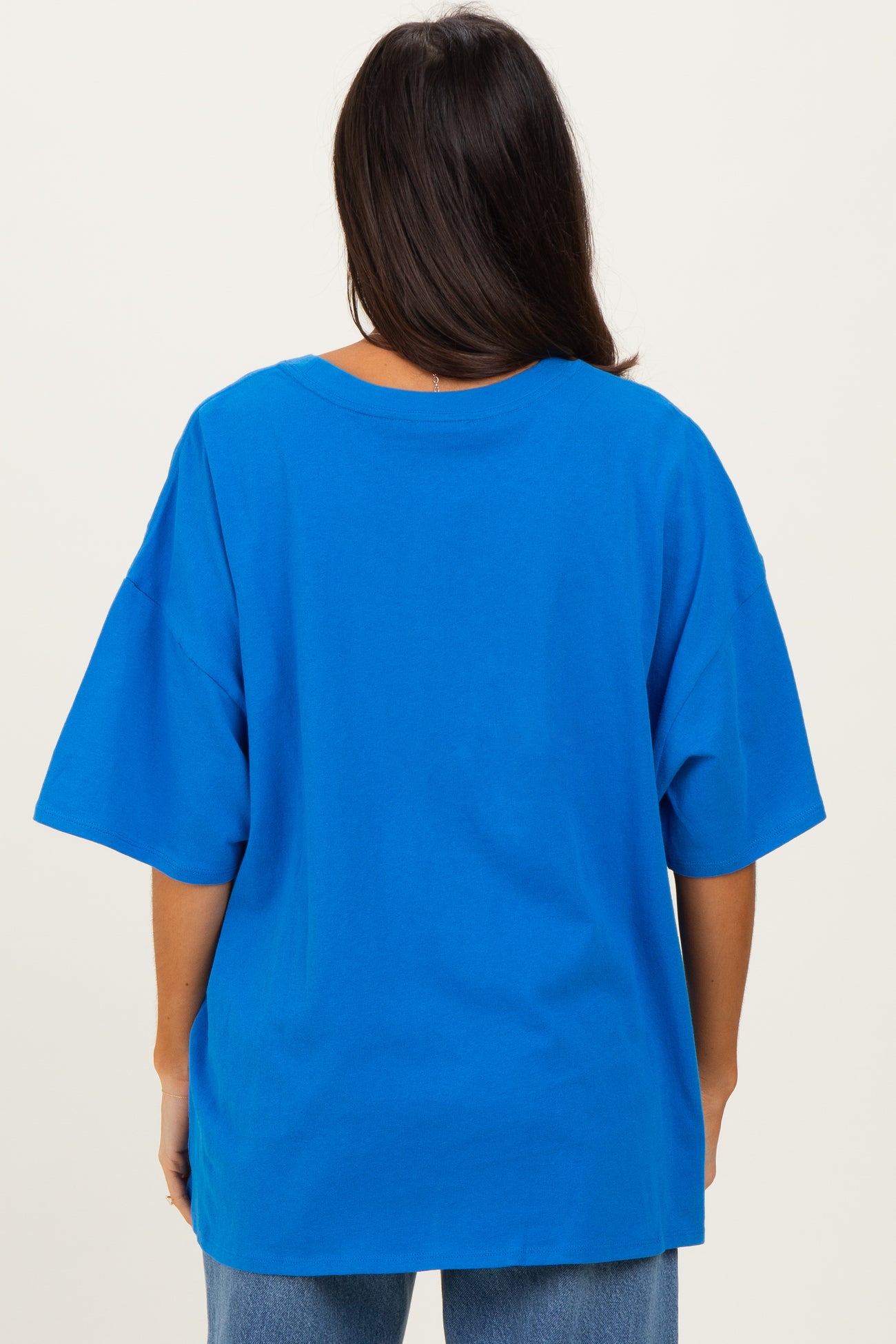 woman wearing a bright blue oversized t-shirt, viewed from the back, paired with light denim jeans