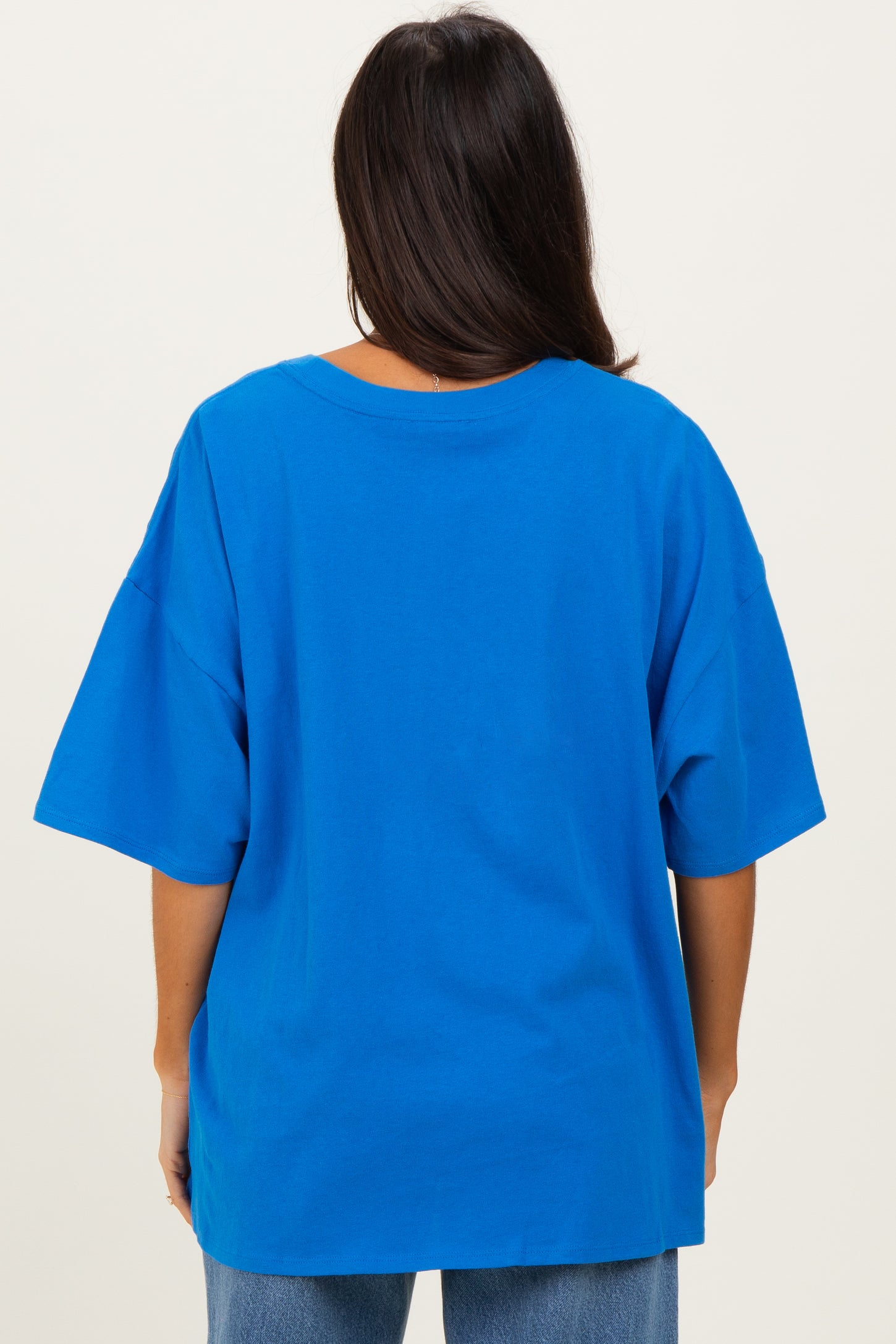 woman wearing a bright blue oversized t-shirt, viewed from the back, paired with light denim jeans