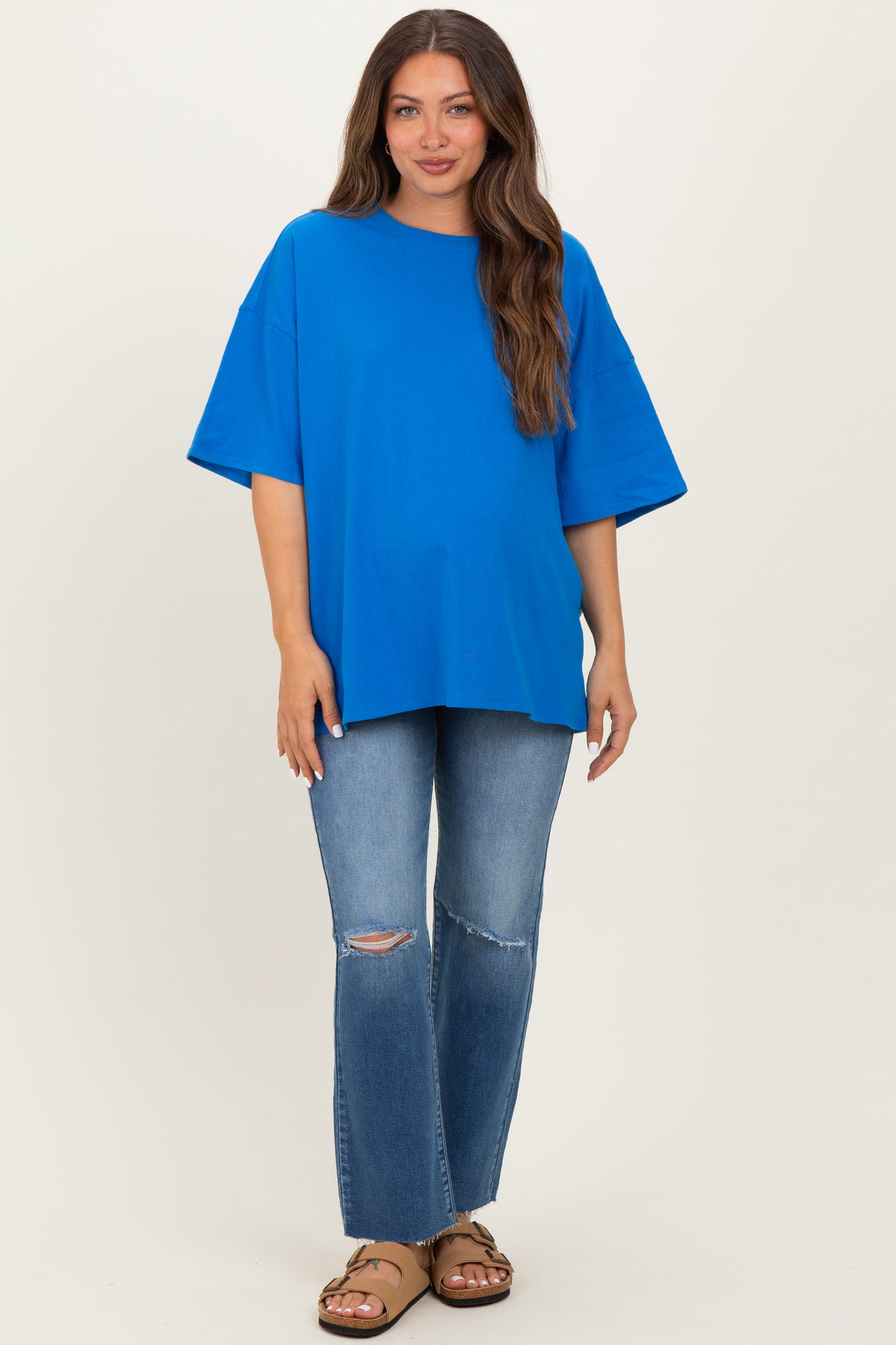 woman wearing a bright blue oversized maternity top and distressed jeans, showing her baby bump