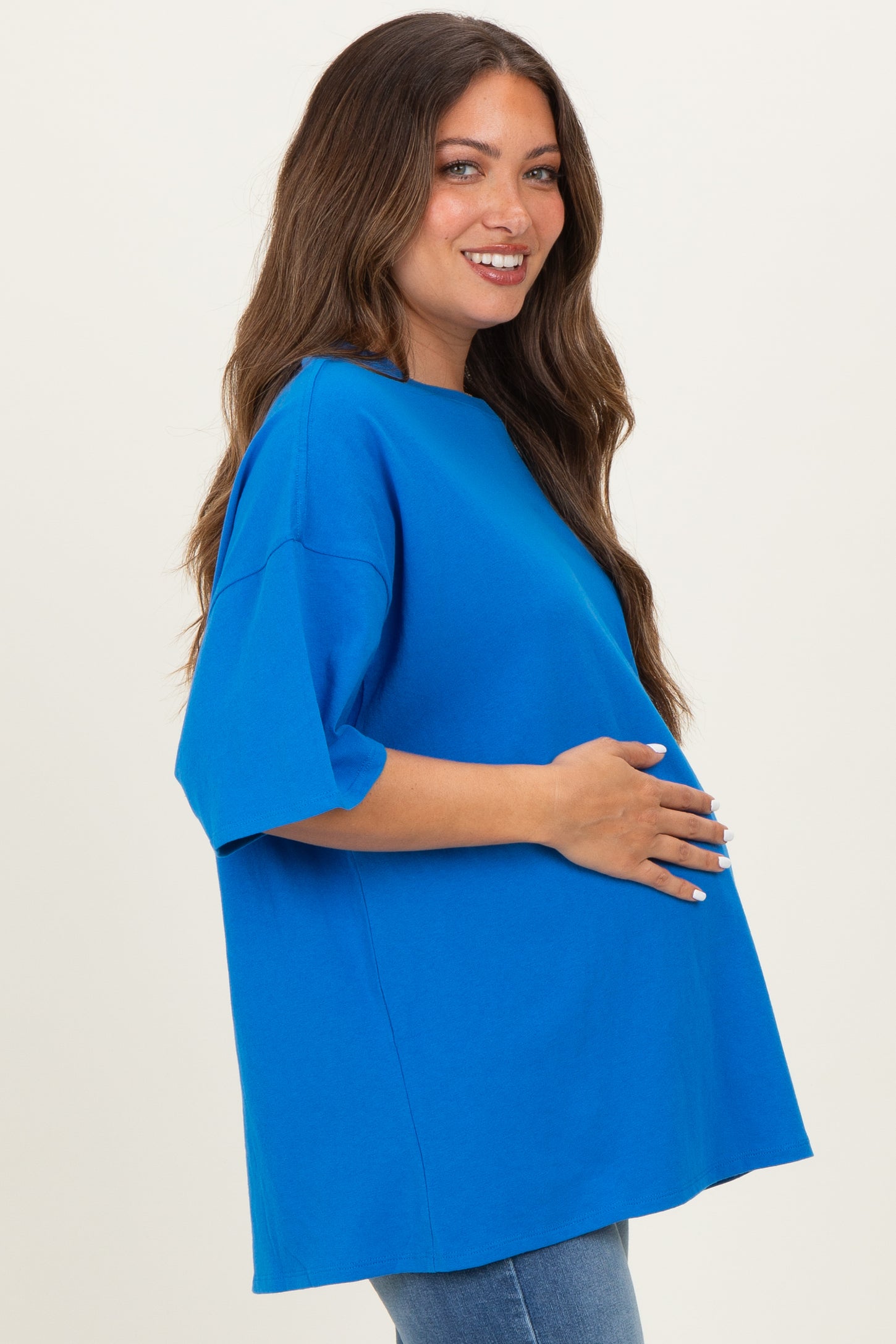 woman wearing a bright blue oversized maternity top and holding her baby bump