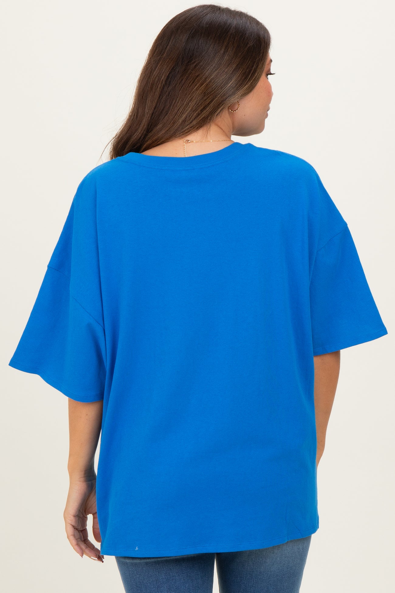 woman wearing a bright blue oversized maternity t-shirt from the back, styled with casual jeans