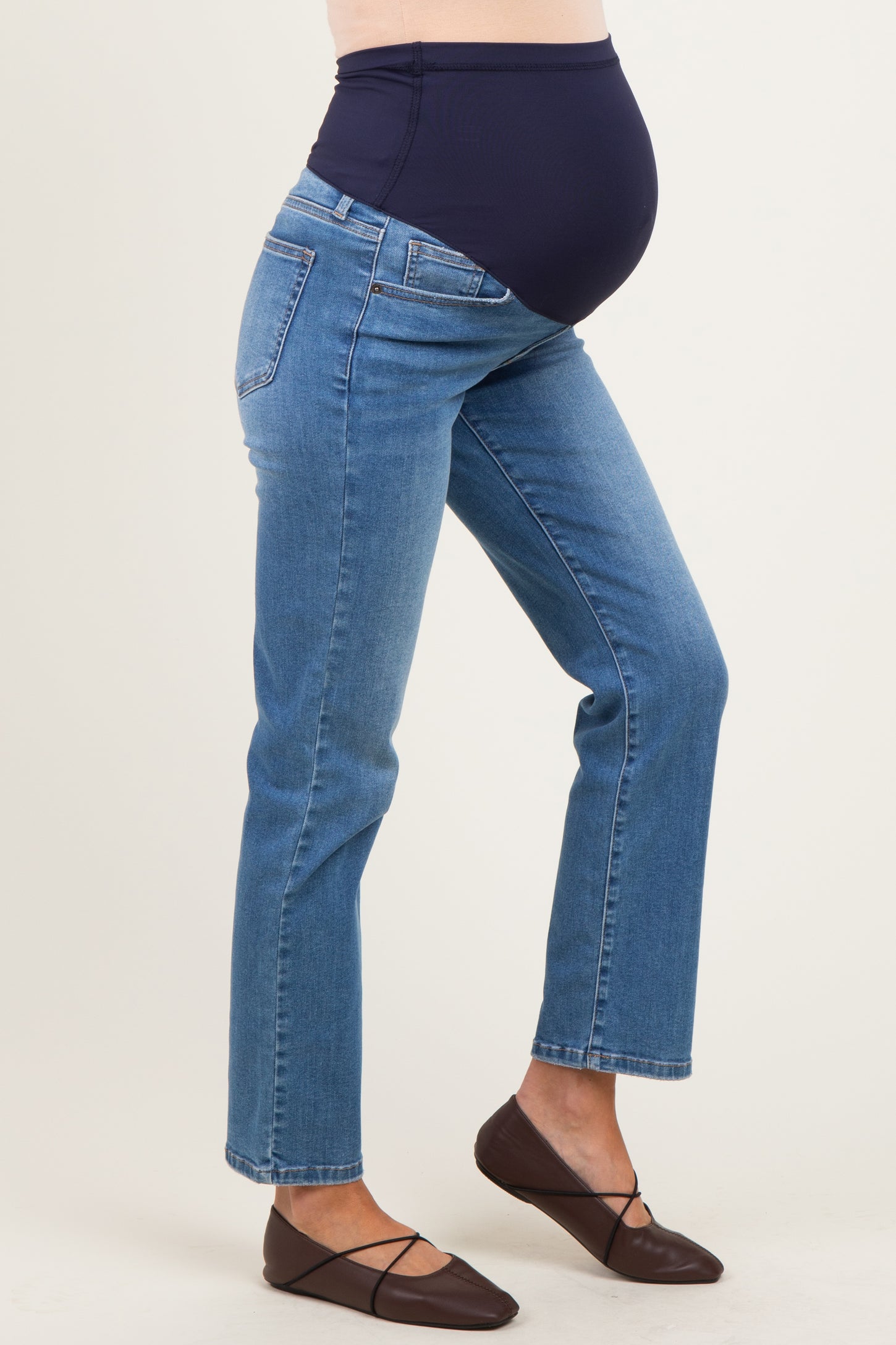 woman wearing dark blue maternity jeans with a supportive belly panel and flat shoes, showing a visible baby bump