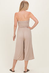 woman wearing a taupe strapless jumpsuit with a gathered bodice and wide leg cropped pants, viewed from the back