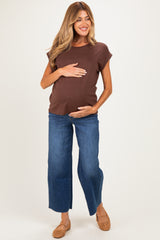 woman wearing a brown short sleeve maternity top and blue wide-leg jeans, gently holding her baby bump