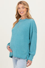 woman wearing a teal ribbed maternity sweater and holding her baby bump, paired with light wash jeans