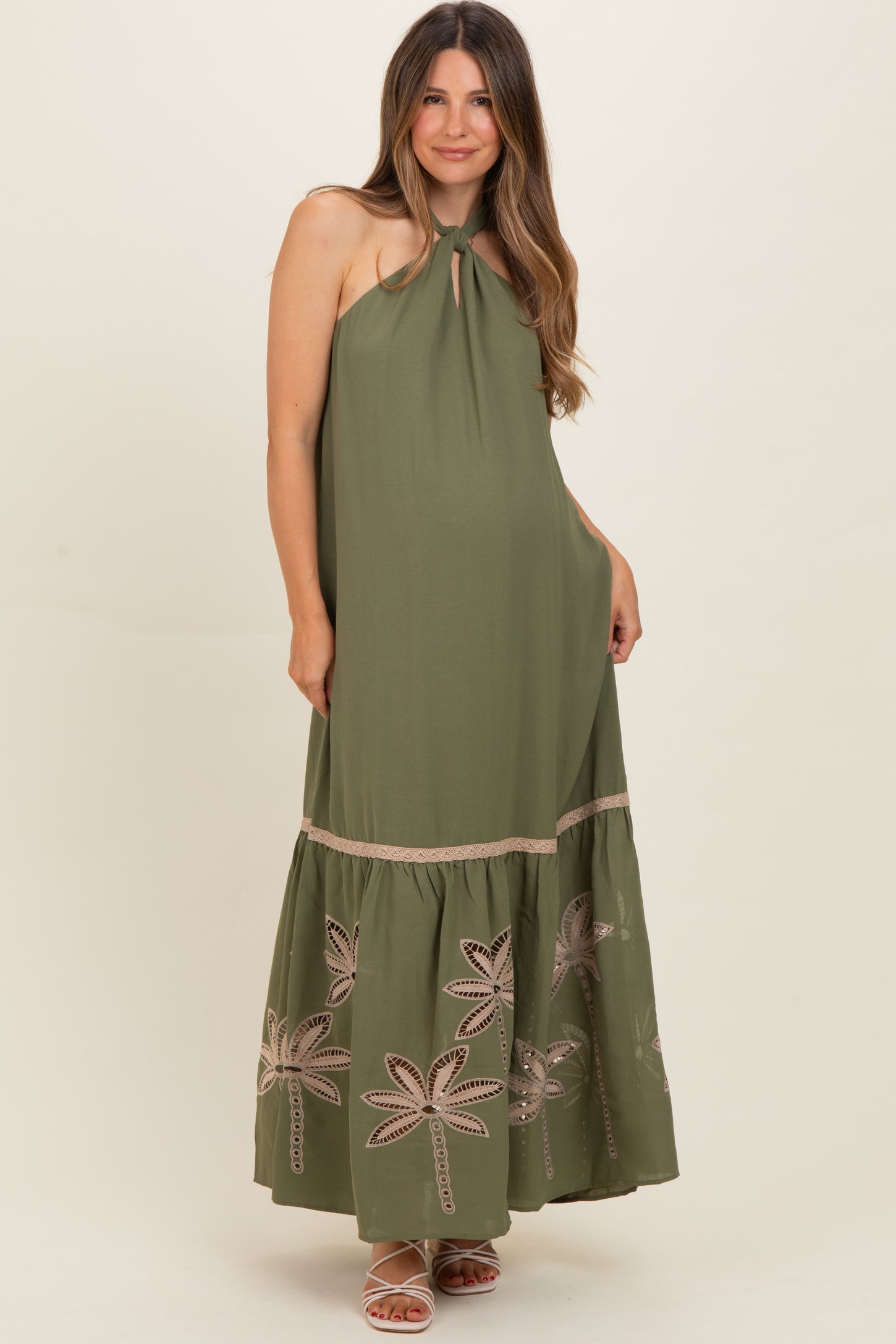 woman wearing an olive green halter neck maternity dress with embroidered palm leaf details and a flowy skirt