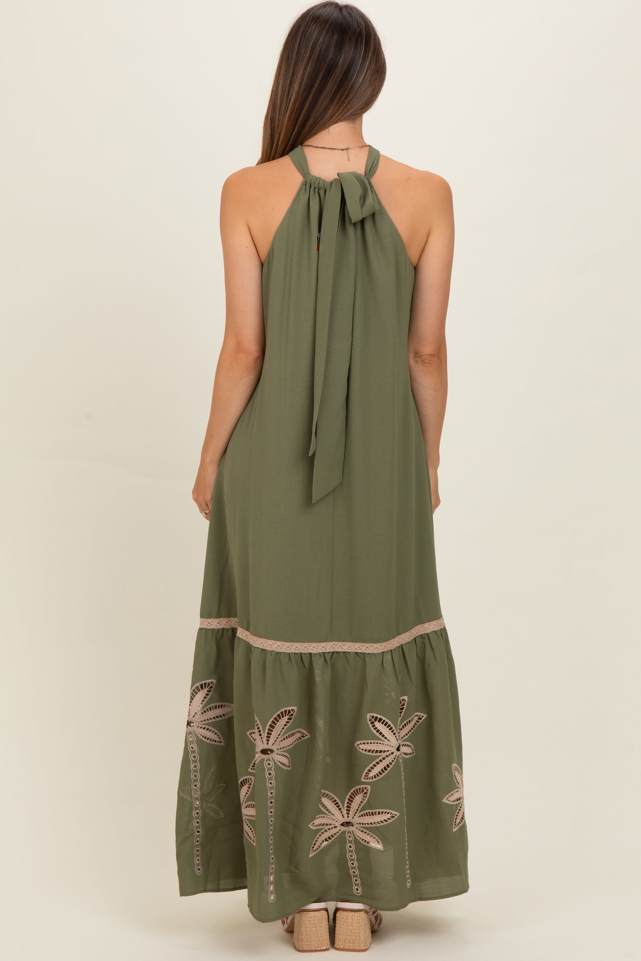 woman wearing an olive green maternity maxi dress with a halter neck and palm tree embroidery on the skirt