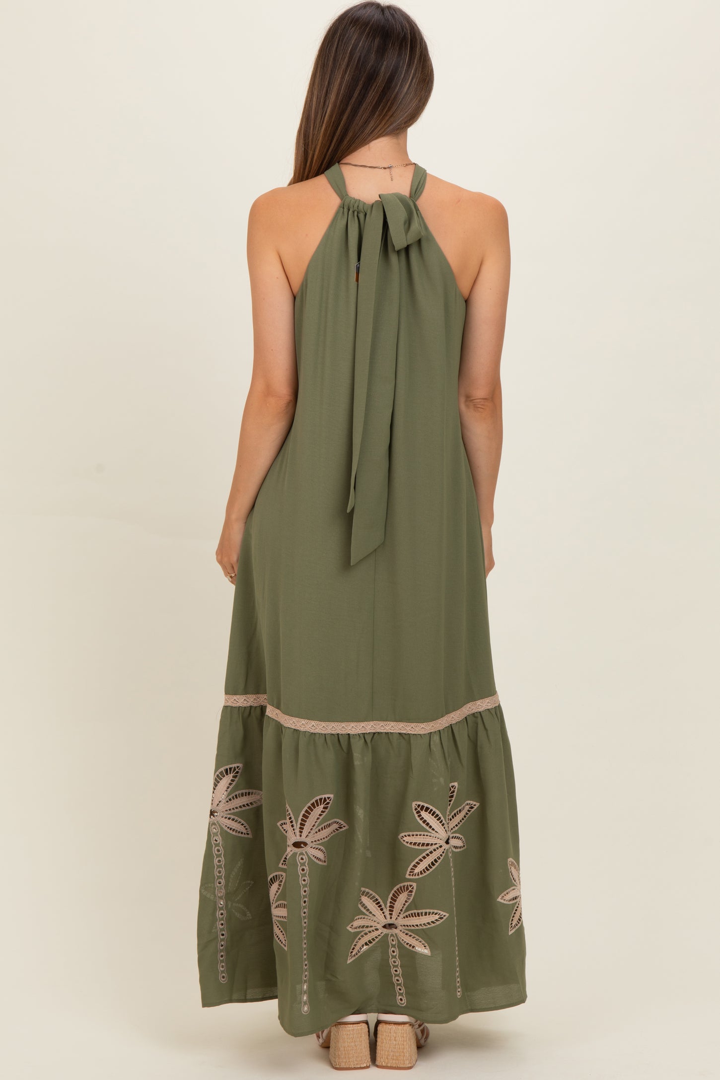 woman wearing an olive green maternity maxi dress with a halter neck and palm tree embroidery on the skirt