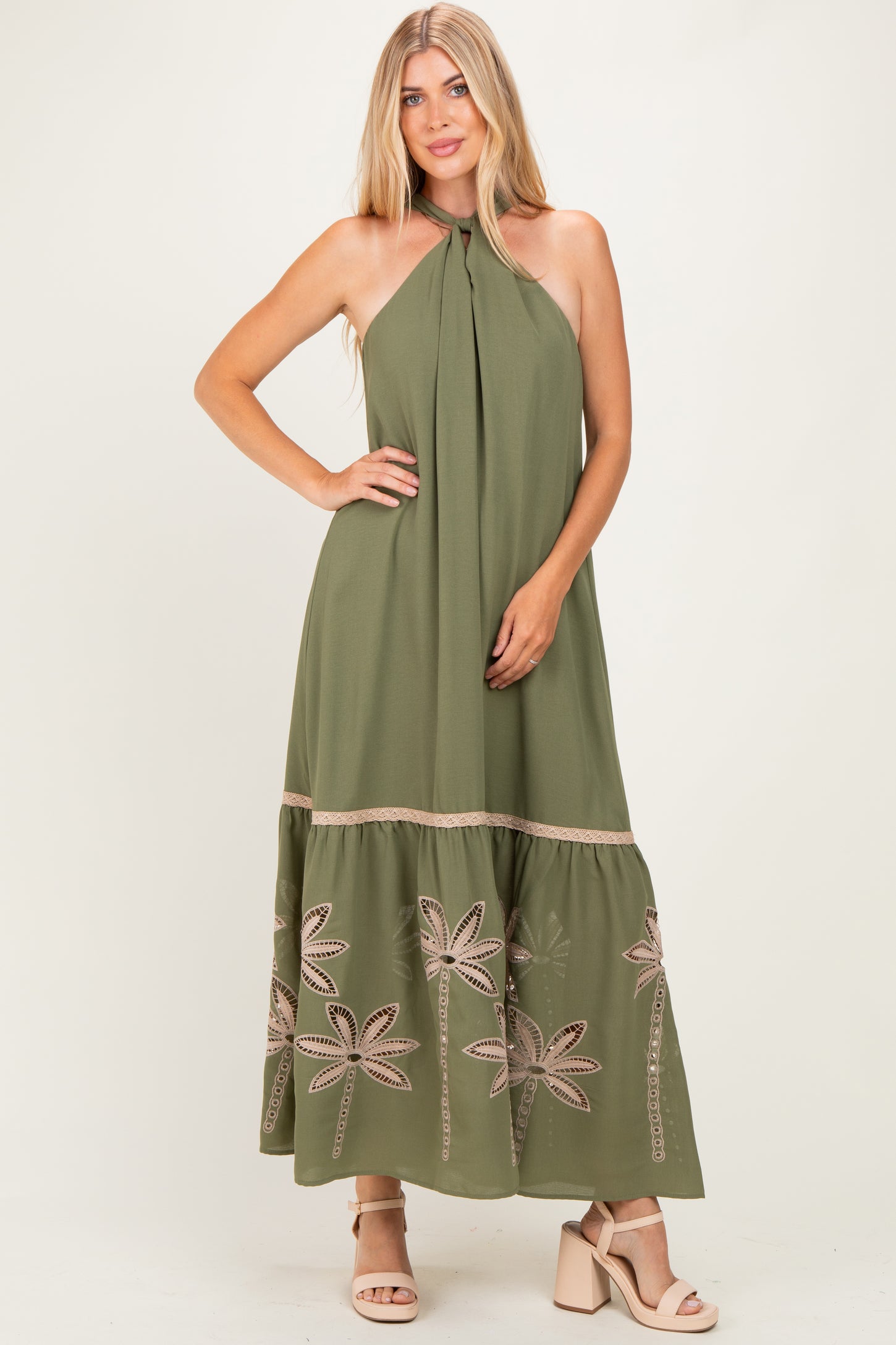 woman wearing an olive green maxi dress with halter neck and floral embroidery at the hem