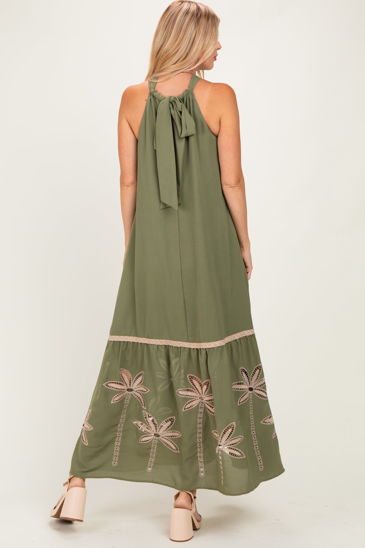 woman wearing an olive green maxi dress with embroidered palm trees and a bow tie detail at the back