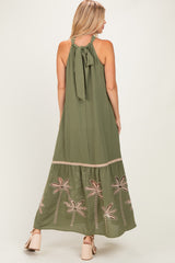 woman wearing an olive green maxi dress with embroidered palm trees and a bow tie detail at the back