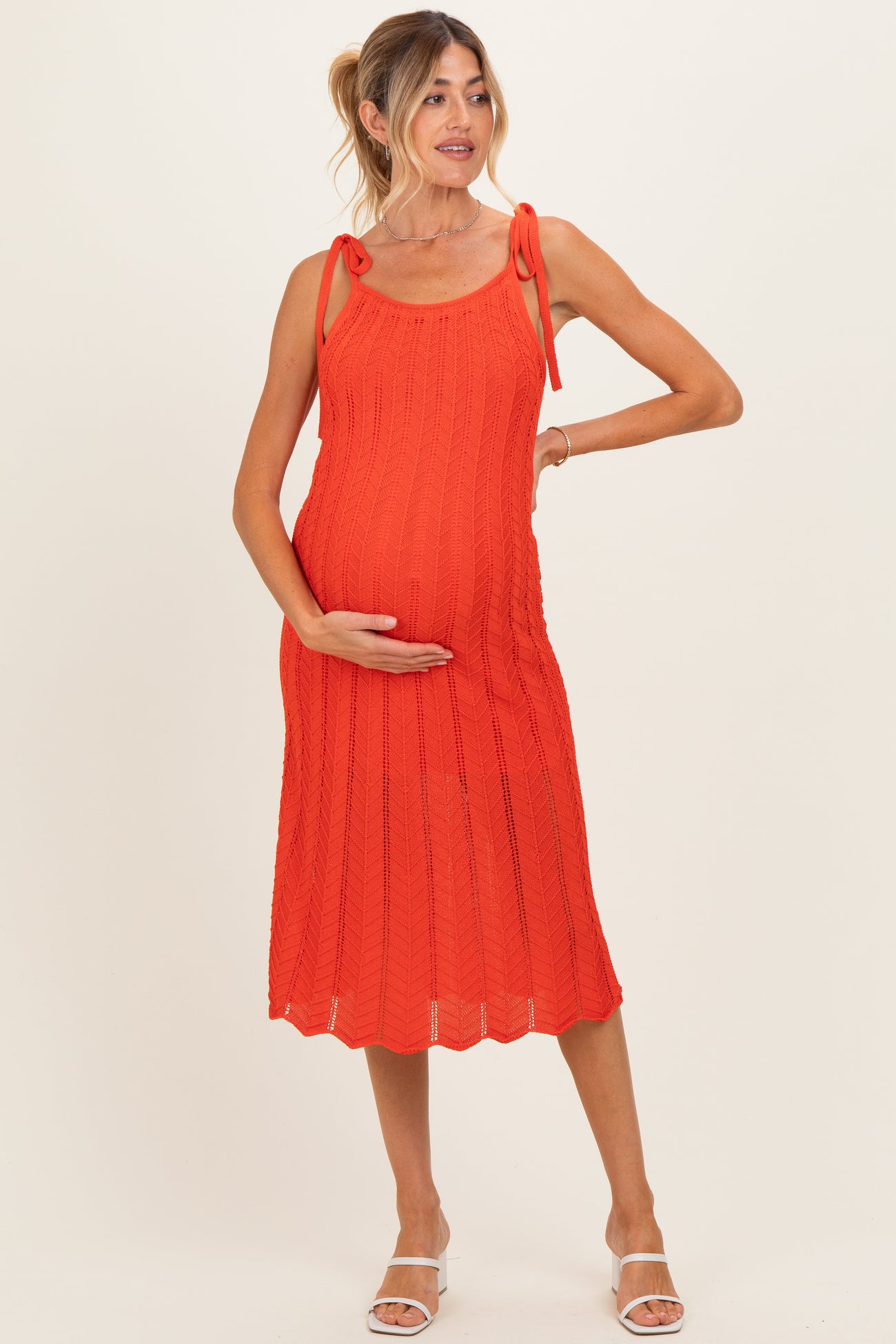 woman wearing a vibrant orange sleeveless maternity dress with tie straps and a visible baby bump