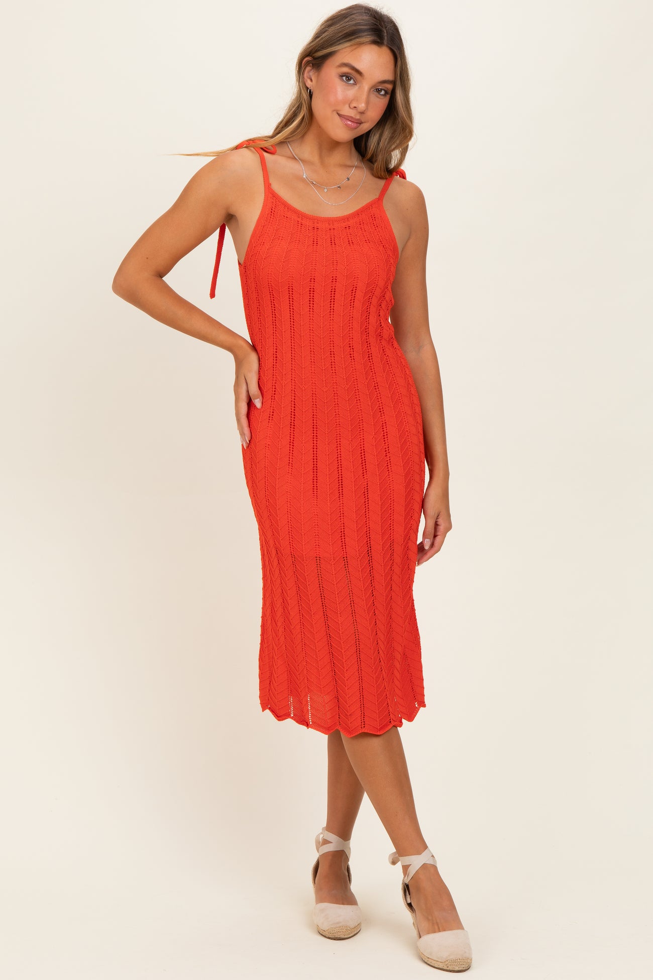woman wearing a bright red knitted midi dress with tie straps and ribbed texture, posing elegantly