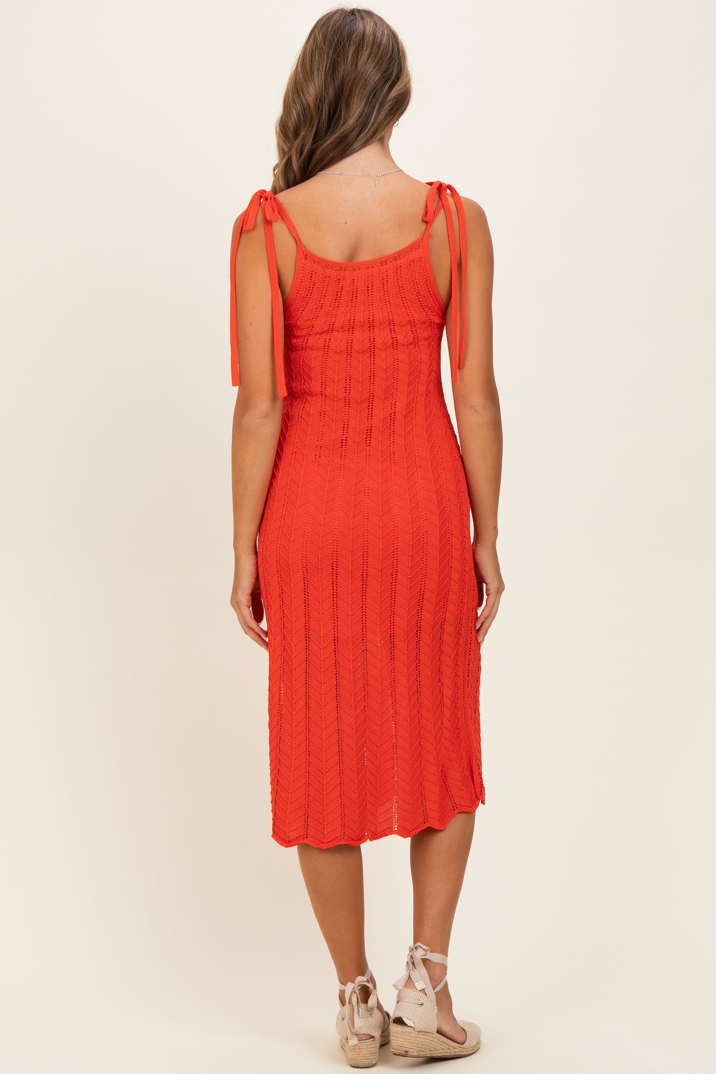 woman wearing a coral knee-length knit dress with tie straps, showcased from the back