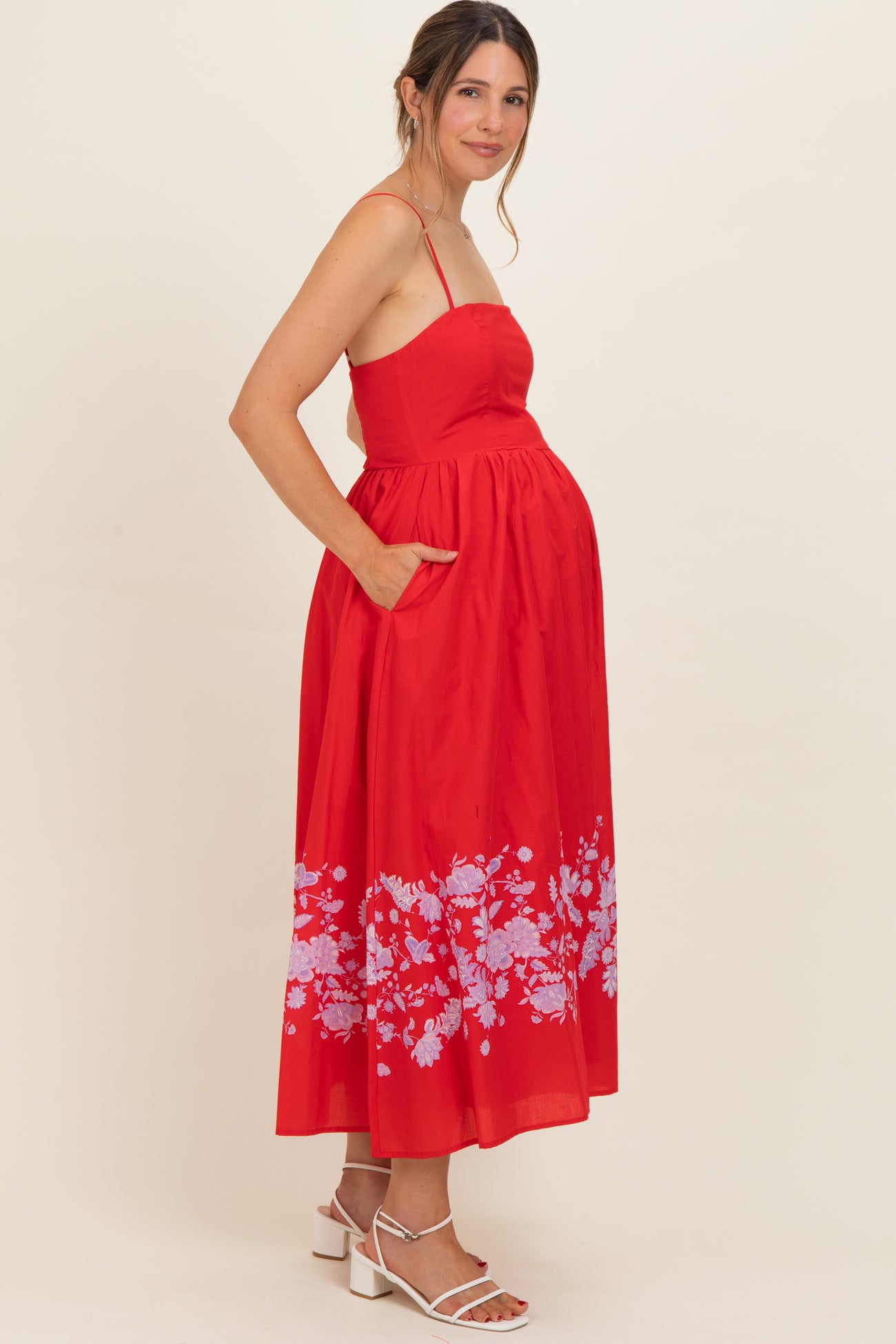 woman wearing a red maternity dress with floral print and pockets, showing her baby bump