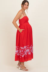 woman wearing a red maternity dress with floral print and pockets, showing her baby bump