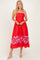 woman wearing a red midi dress with floral print at the hem and thin straps, smiling and standing on a plain background