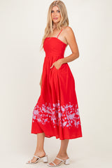 woman wearing a red midi dress with floral print and spaghetti straps, styled with pockets and a flowy skirt