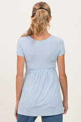 woman wearing a light blue maternity top with a fitted bodice and gathered waist, showing the back view