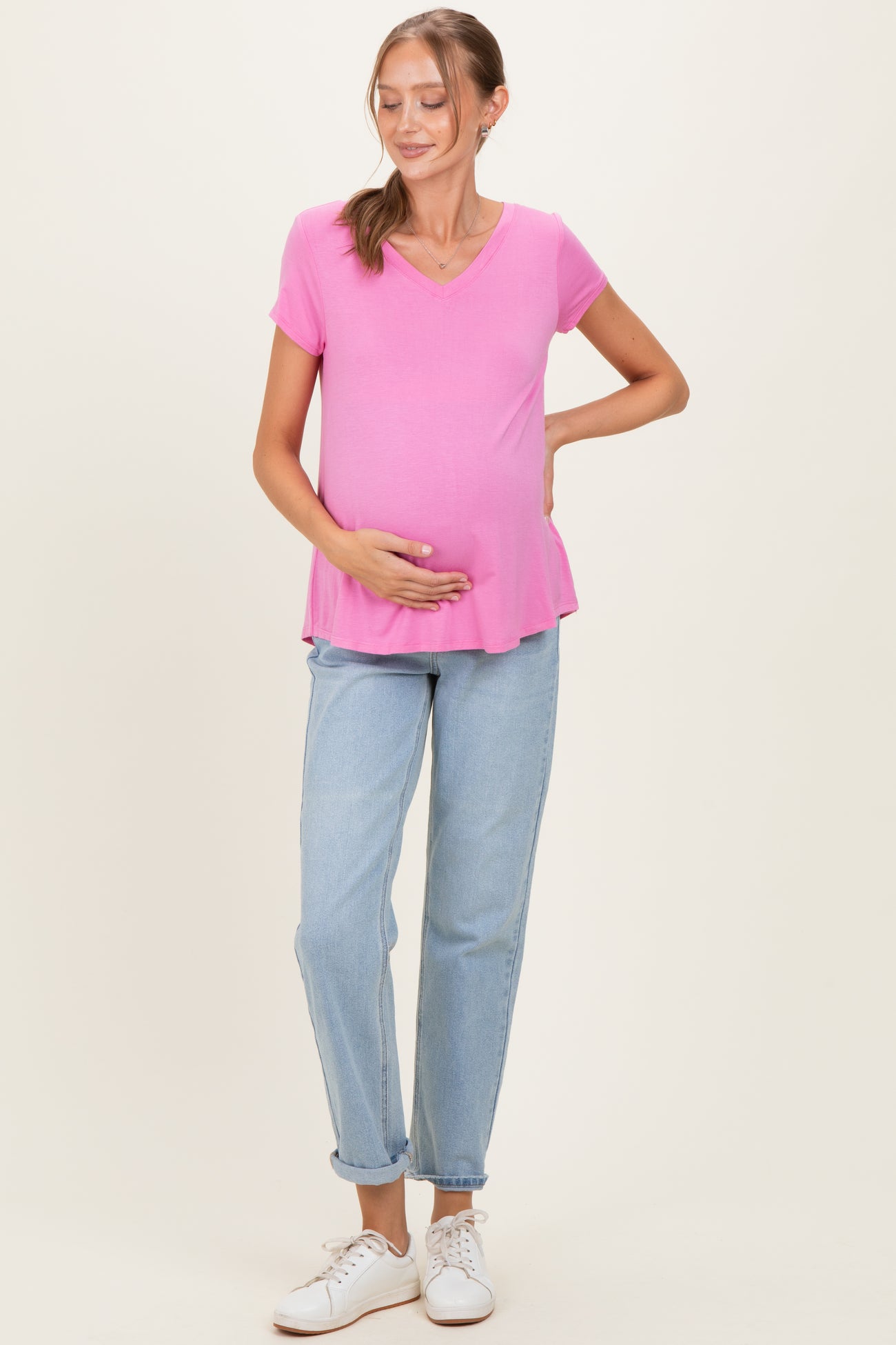 woman wearing a pink short sleeve maternity top and holding her baby bump, paired with light blue jeans