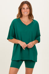 woman wearing a green oversized v-neck t-shirt and matching green bike shorts, smiling at the camera