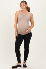 woman wearing a nude maternity tank top and black leggings, gently holding her baby bump