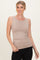 woman wearing a beige sleeveless fitted top and black jeans, smiling at the camera