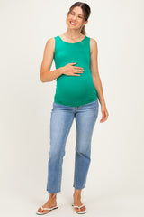 woman wearing a green maternity tank top and blue jeans, holding her baby bump