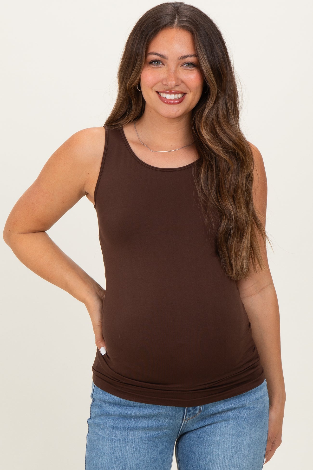 woman wearing a brown maternity tank top and showing her baby bump while smiling