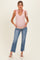 woman wearing a light pink maternity tank top with bow straps and blue distressed cropped jeans, holding her baby bump