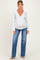 woman wearing a gray long sleeve wrap maternity top and blue wide leg jeans, showing her baby bump