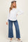 woman wearing a white long sleeve maternity top and blue wide leg jeans, showing her baby bump, styled with a hat