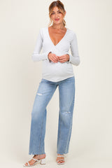 woman wearing a light gray long sleeve maternity top with a deep v-neck and distressed wide-leg jeans, holding baby bump