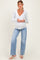 woman wearing a light gray long sleeve maternity top with a deep v-neck and distressed wide-leg jeans, holding baby bump