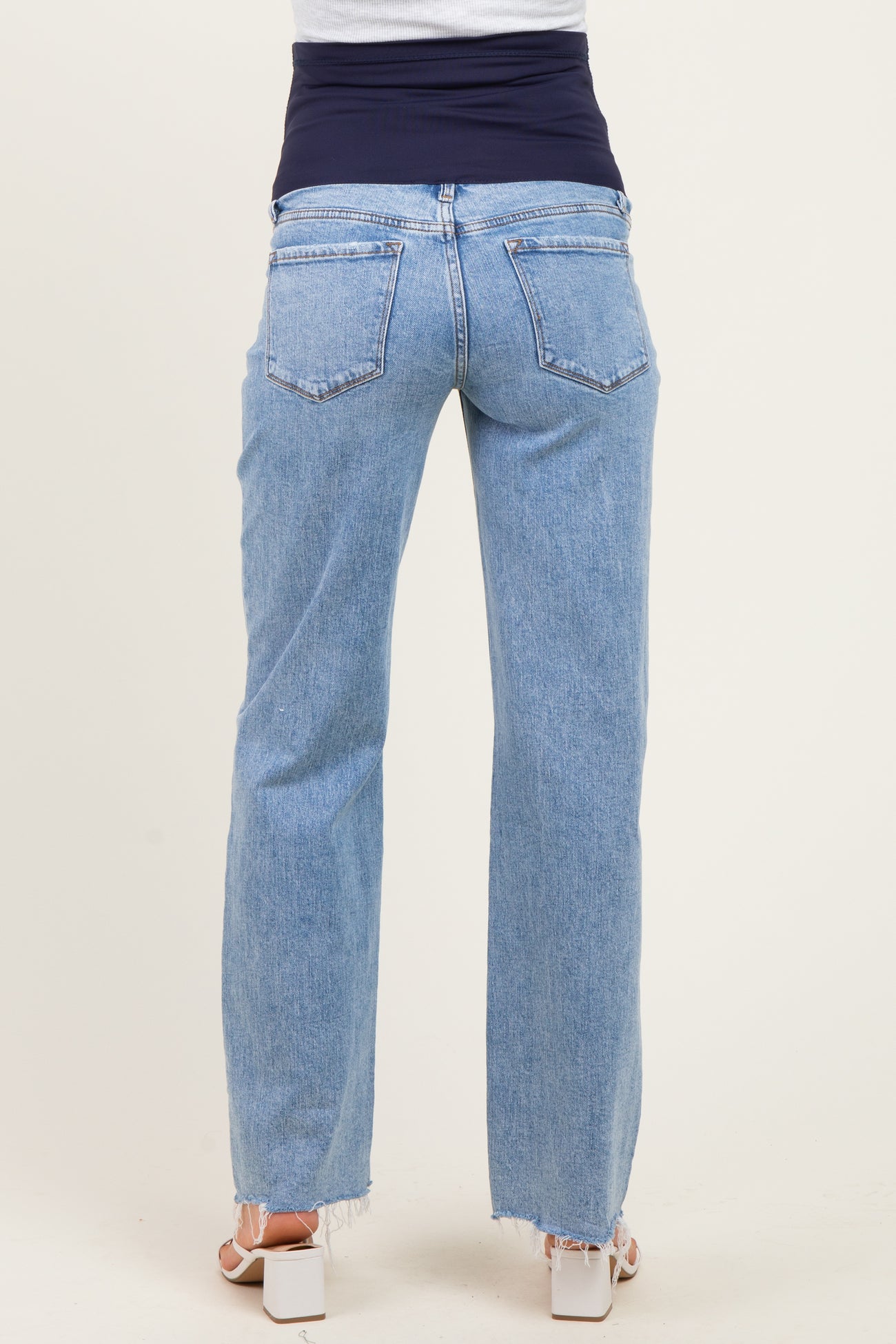 woman wearing light blue maternity jeans with a dark blue over-the-bump waistband, showing a relaxed fit and frayed hem