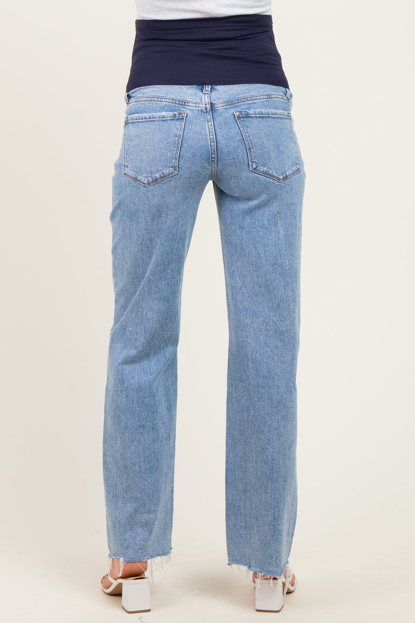 woman wearing light blue maternity jeans with a dark blue over-the-bump waistband, showing a relaxed fit and frayed hem