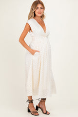 woman wearing a white maternity dress with black polka dots and pockets, displaying her baby bump