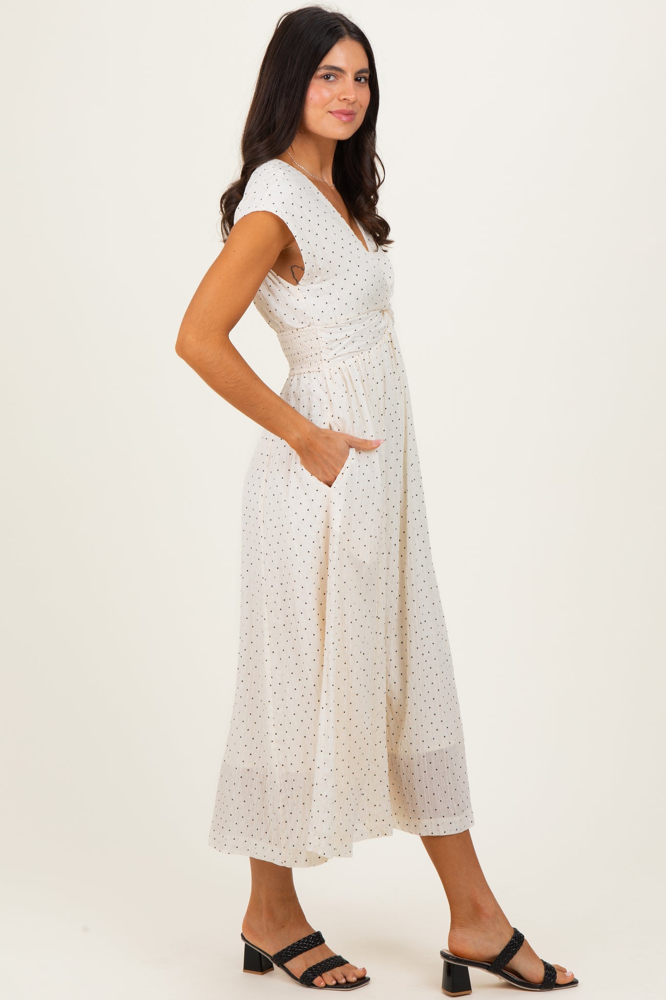 woman wearing a white midi dress with black polka dots and pockets, styled with black sandals
