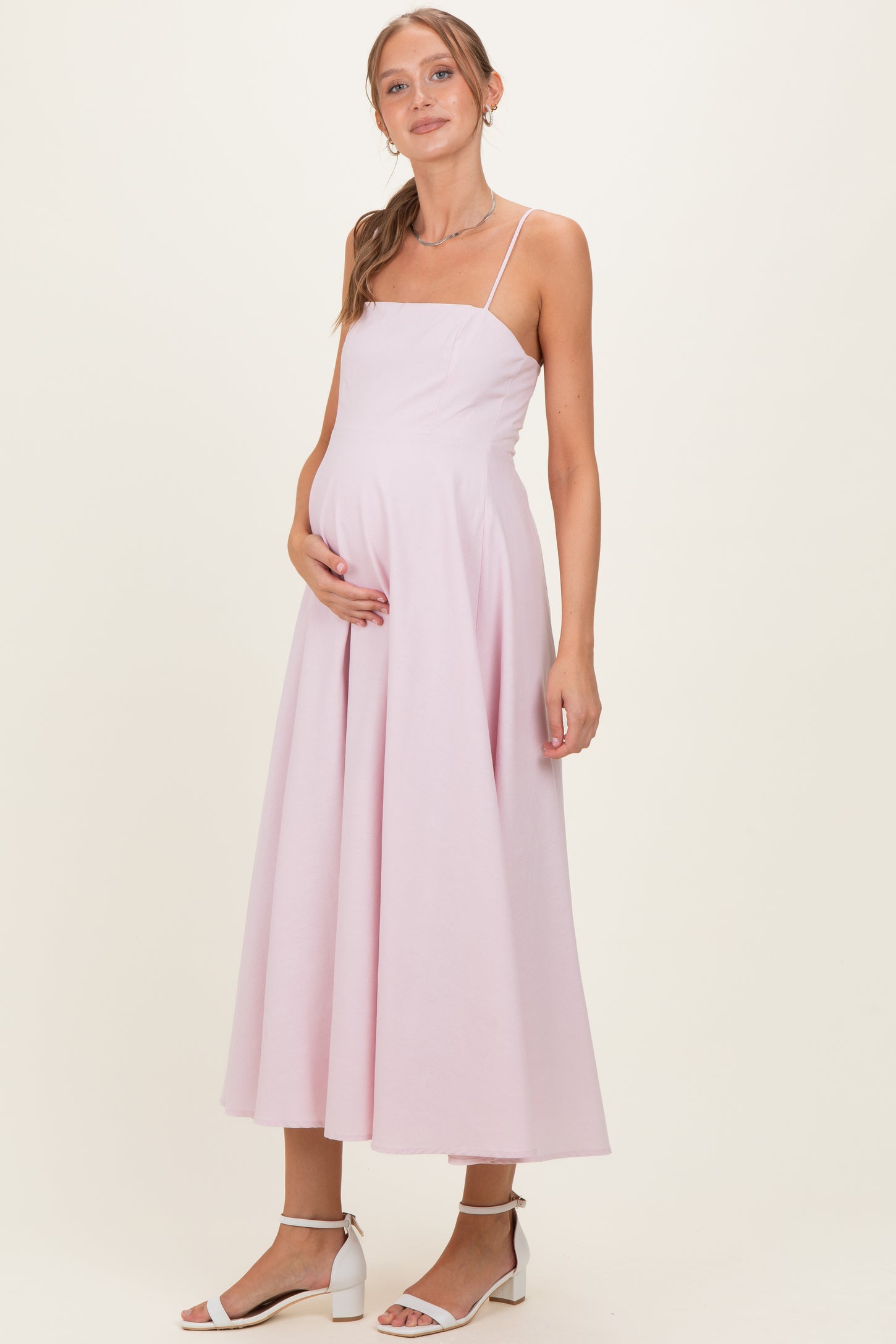 woman wearing a light pink maternity gown with a fitted bodice and flowing skirt, holding her baby bump