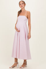 woman wearing a light pink maternity gown with a fitted bodice and flowing skirt, holding her baby bump