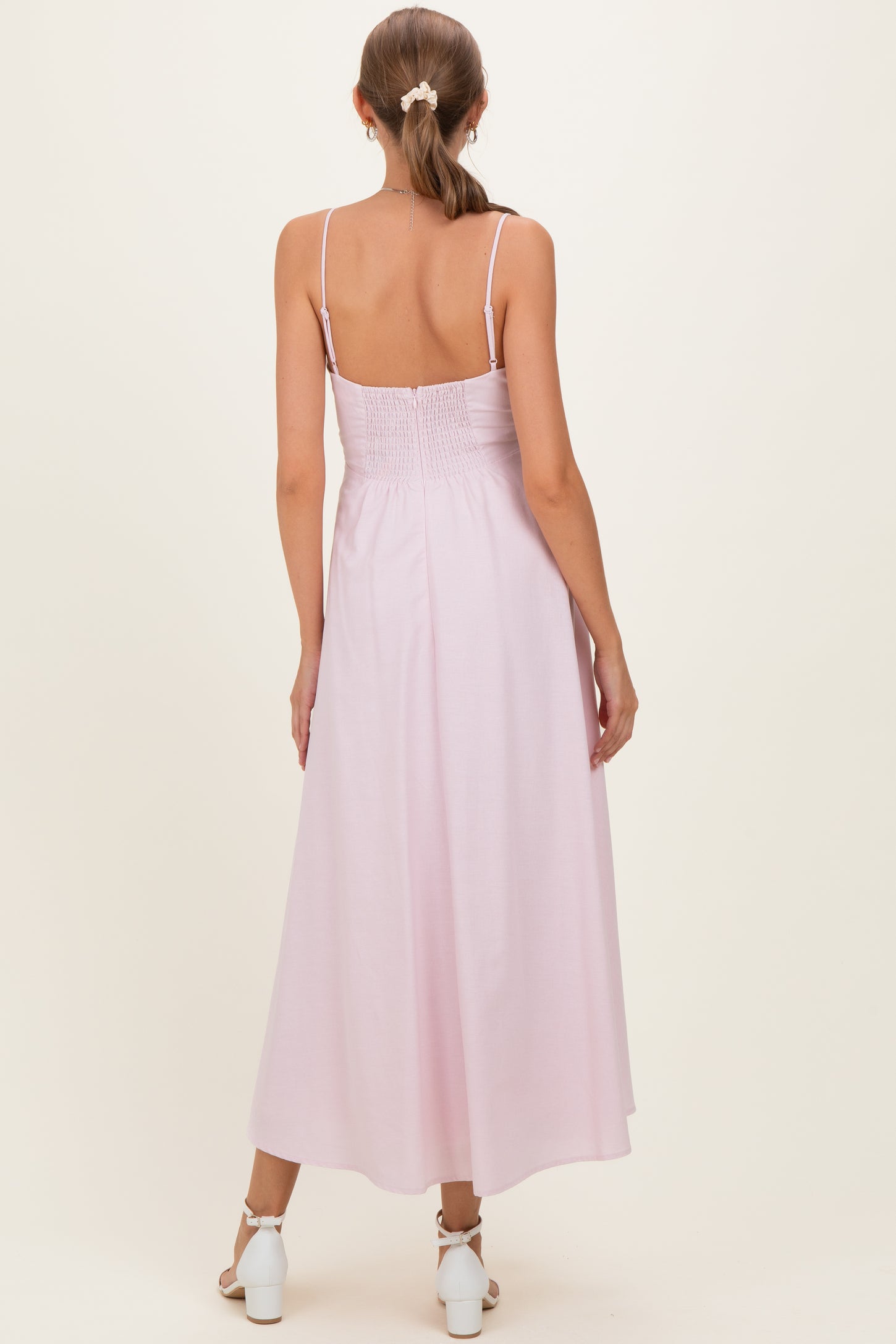 woman wearing a light pink maternity maxi dress with spaghetti straps and smocked back, standing with her back to the camera