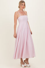woman wearing a light pink spaghetti strap midi dress with a flowy skirt and white block heel sandals