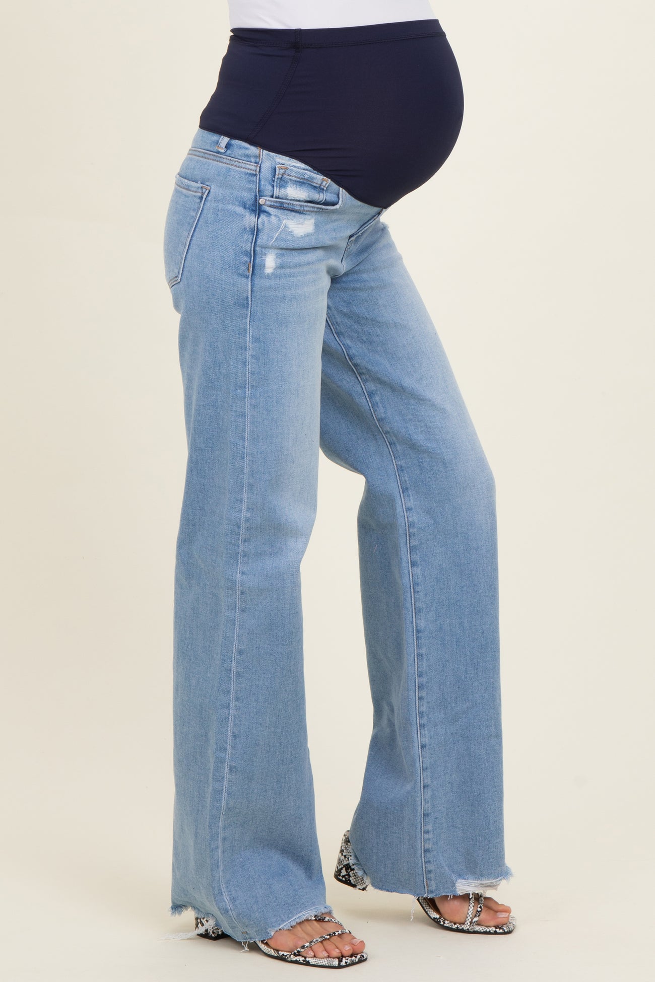 woman wearing light blue maternity flared jeans with a dark blue over-the-bump waistband and a visible baby bump