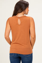 woman wearing a rust-colored sleeveless maternity top with a keyhole back and braided detail, facing away from the camera