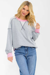 woman wearing a light gray sweatshirt with pink accents and relaxed sleeves, paired with blue jeans