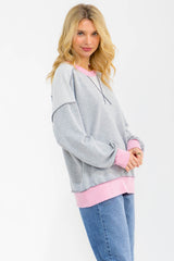 woman wearing a gray and pink color-blocked sweatshirt with long sleeves and a relaxed fit, paired with blue jeans
